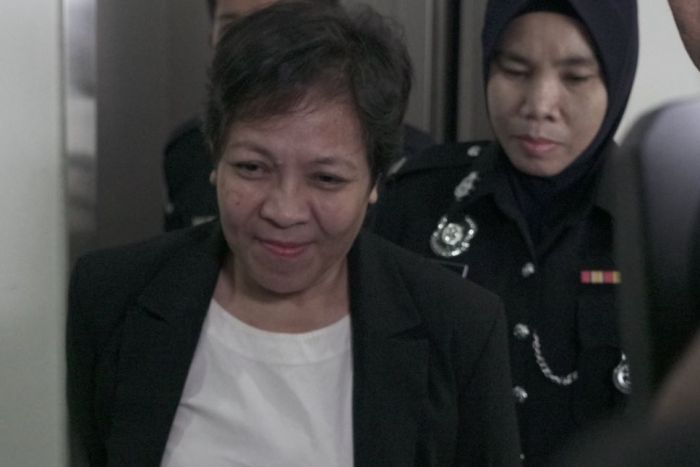 Maria Exposto smiles slightly as she is escorted into a Malaysian court by authorities. 
