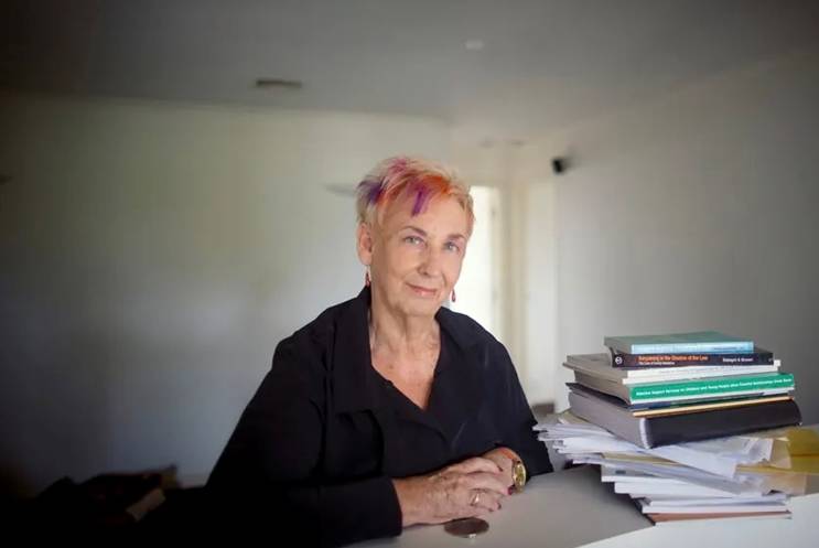 A photo of Thea Brown sitting at a desk next to a stack of books