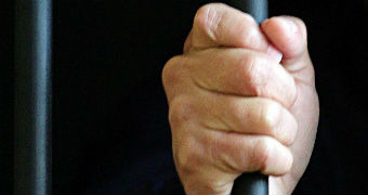 A hand grips a bar of a prison cell.