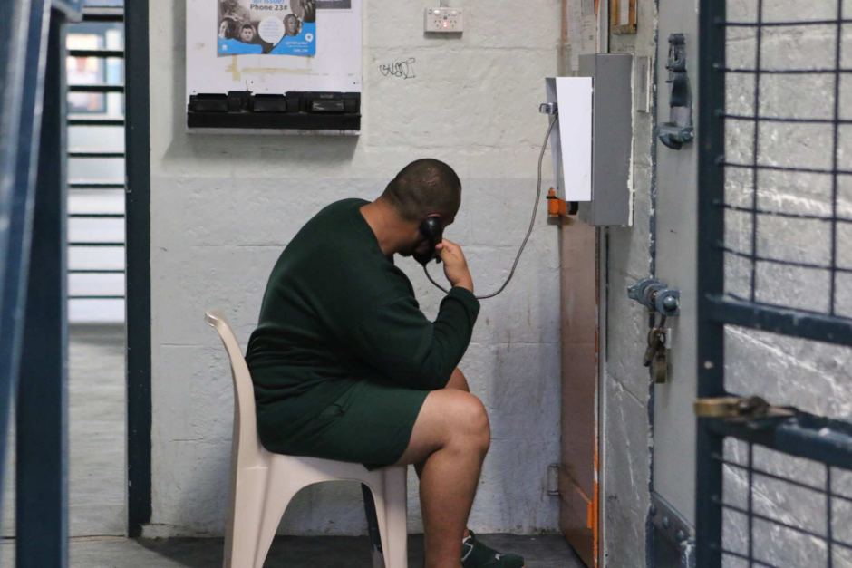 An inmate sits on a chair talking on a landline telephone.