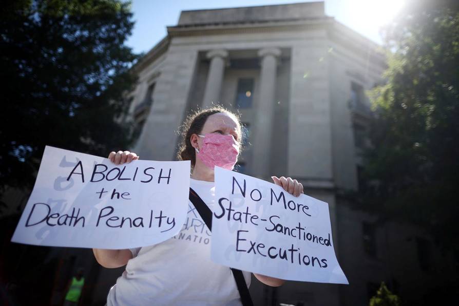 A woman wearing a Covid-19 face mask holds two signs, one reading Abolish the death penalty, the other reading No more state-sanctioned executions.