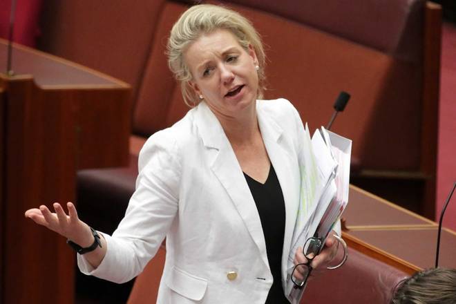 Bridget McKenzie looks across the room and holds her arms in a shrug while also carrying binders